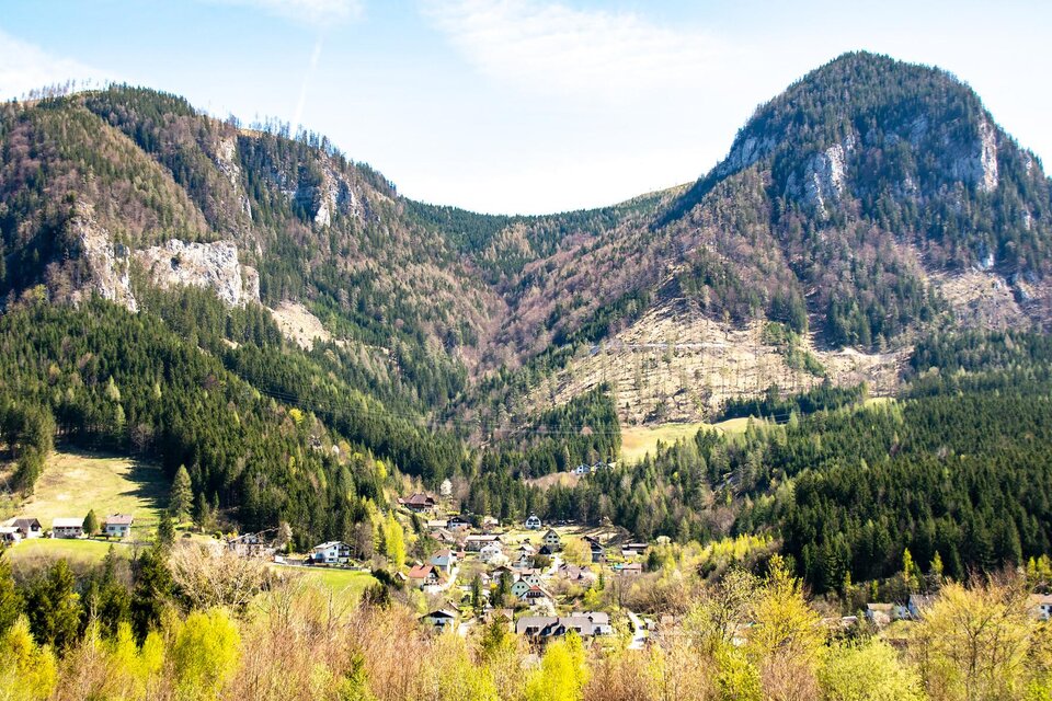 Eine malerische Berglandschaft mit grünen Wäldern und sanften Hügeln. Im Vordergrund liegt ein kleines Dorf, umgeben von majestätischen Bergen. | © TV Gesäuse