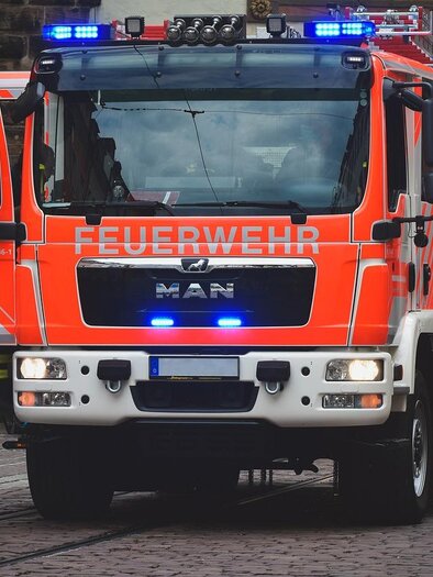 Ein leuchtend orangefarbenes Feuerwehrfahrzeug mit Blaulicht steht auf einer Straße. Die Tür des Fahrzeugs ist geöffnet und es ist bereit für den Einsatz. | © pixabay.com