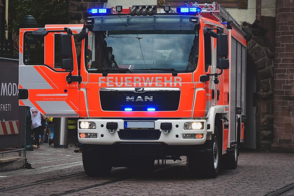 Ein leuchtend orangefarbenes Feuerwehrfahrzeug mit Blaulicht steht auf einer Straße. Die Tür des Fahrzeugs ist geöffnet und es ist bereit für den Einsatz. | © pixabay.com