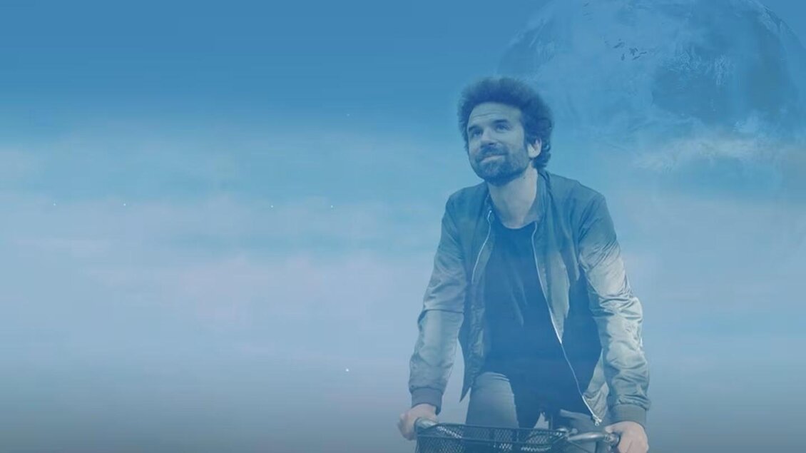 Ein Mann fährt lächelnd mit dem Fahrrad. Der Hintergrund ist klar und hat einen blauen Farbton. | © Cyril Dion - Ott
