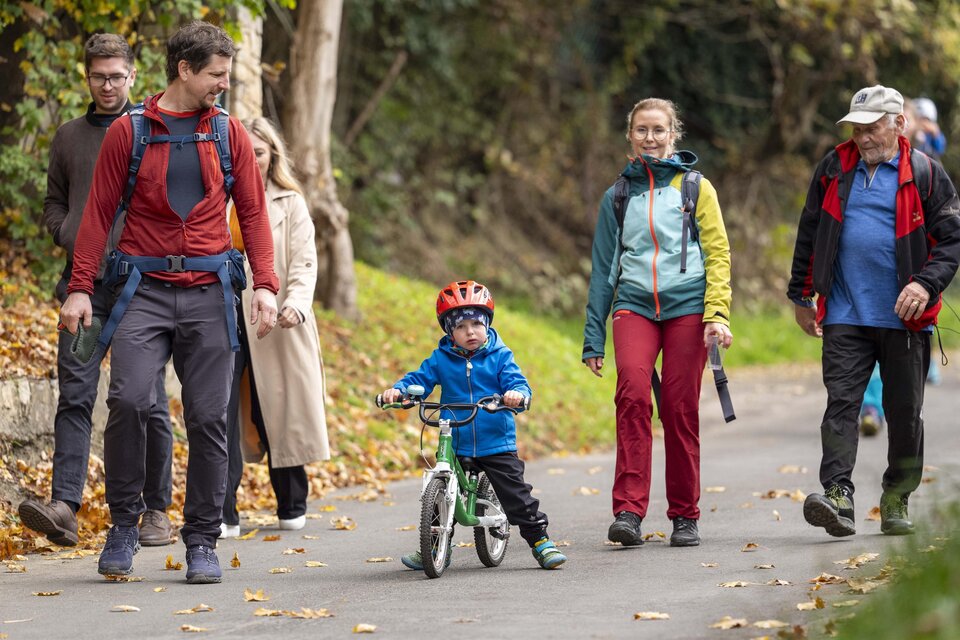 Eine Gruppe von Menschen geht auf einem Weg, während ein Kind auf einem kleinen Fahrrad fährt. Die Umgebung ist herbstlich mit buntem Laub. | © Stadtgemeinde Leoben