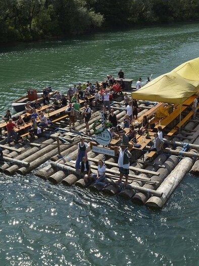 Eine große Floßfahrt mit vielen Menschen auf einem Fluss. Es gibt Sitzplätze und ein Dachschutz für Schatten. | © Floß & Co