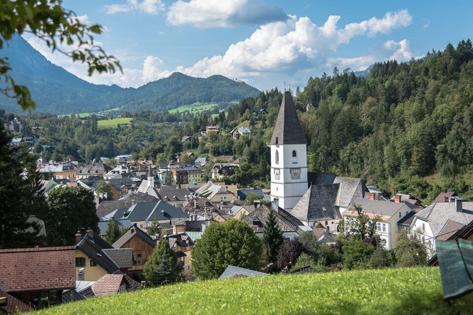 Die malerische Aussicht von der Tauscherin, einem Ausflugsziel in Bad Aussee. Das Bild zeigt den Blick von oben auf die Kurstadt Bad Aussee mit der Pfarrkirche und dem Stadtkern, umgeben von der grünen Landschaft und den Bergen des Ausseerlandes. Der Himmel ist blau und leicht von Wolken duchzogen. | © Herbert Sams