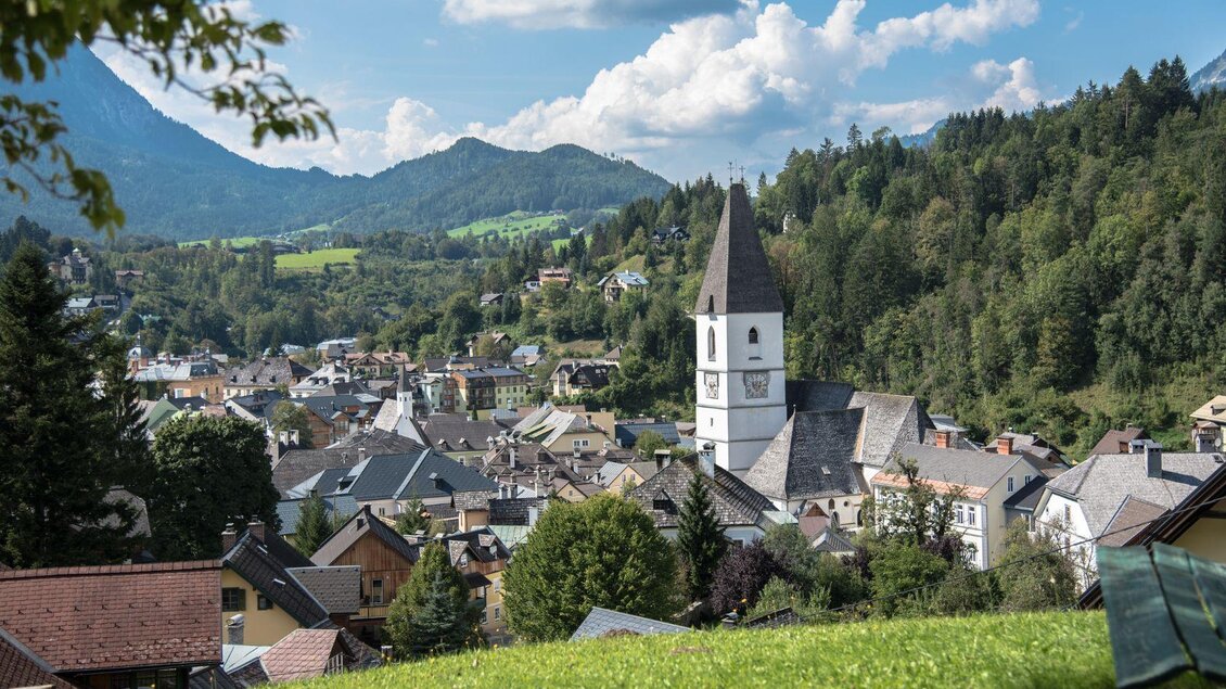 Die malerische Aussicht von der Tauscherin, einem Ausflugsziel in Bad Aussee. Das Bild zeigt den Blick von oben auf die Kurstadt Bad Aussee mit der Pfarrkirche und dem Stadtkern, umgeben von der grünen Landschaft und den Bergen des Ausseerlandes. Der Himmel ist blau und leicht von Wolken duchzogen. | © Herbert Sams