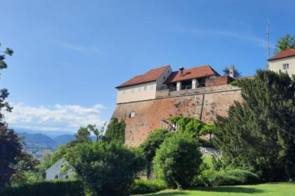 Eine alte Burg steht auf einem Hügel, umgeben von üppigem Grün. Im Hintergrund sind Berge und ein blauer Himmel sichtbar. | © Graz Guides