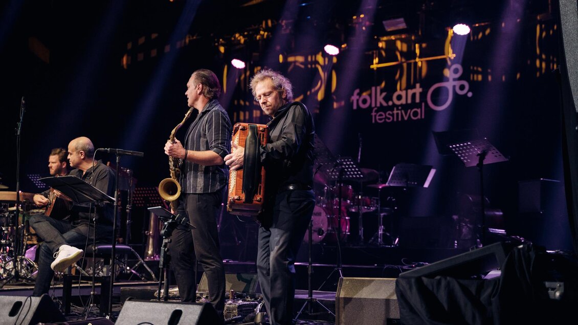 Eine live Band spielt auf einer Bühne beim Folk.Art Festival. Musikinstrumente wie Saxophon und Akkordeon sind zu sehen. | © Madeleine Marie