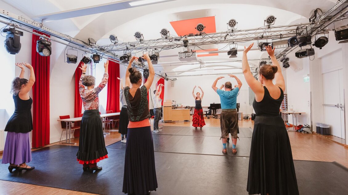 Eine Gruppe von Tänzern übt in einem Raum mit Holzboden und Beleuchtung. Sie tragen Kleidung in verschiedenen Farben und heben die Arme zur Choreografie. | © Madeleine Marie