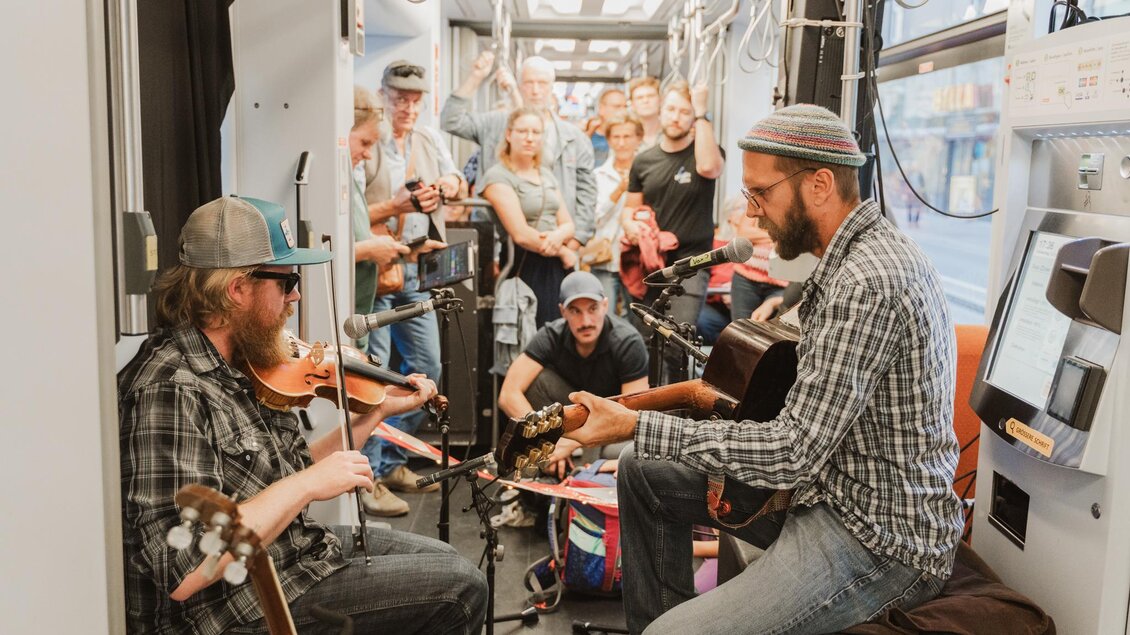 Eine Gruppe von Musikern spielt in einem Zug. Viele Passagiere beobachten die Aufführung aufmerksam. | © Madeleine Marie