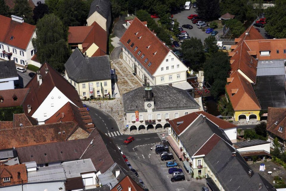 Eine Luftaufnahme eines kleinen Stadtzentrums mit verschiedenen Gebäuden und einem Platz. In der Umgebung sind viele Autos und Bäume zu sehen. | © Rudi Tischler