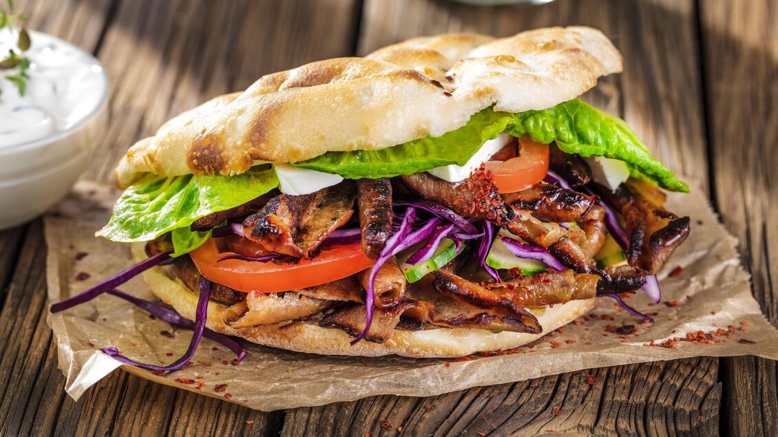 Ein köstliches Sandwich mit gegrilltem Fleisch, frischem Gemüse und knackigem Salat. Serviert auf einem weichen Fladenbrot. | © AdobeStock_133070121
