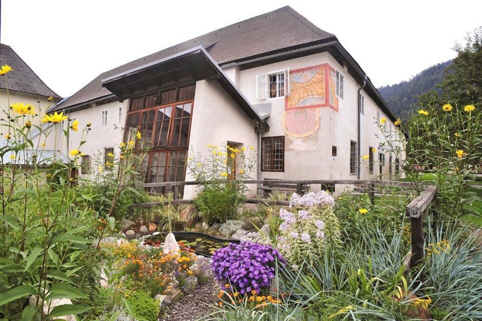 Ein charmantes Gebäude mit einem Garten voller bunter Blumen. Im Hintergrund sind sanfte Hügel zu sehen.