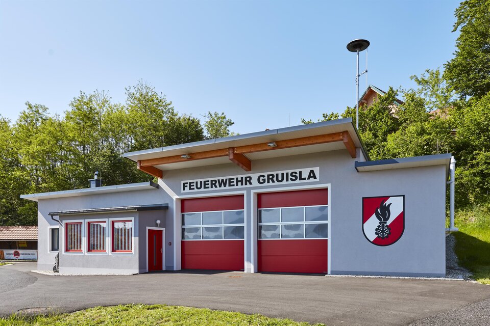 Feuerwehrhaus der Freiwilligen Feuerwehr Gruisla in der Erlebnisregion Thermen- & Vulkanland im Südosten der Steiermark – modernes Feuerwehrgebäude mit roten Toren, umgeben von grüner Natur bei sonnigem Wetter. | © Barbara Majcan