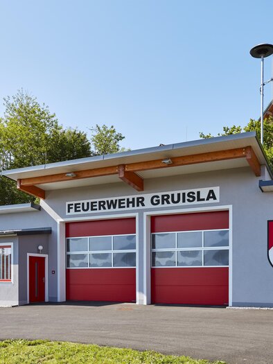 Feuerwehrhaus der Freiwilligen Feuerwehr Gruisla in der Erlebnisregion Thermen- & Vulkanland im Südosten der Steiermark – modernes Feuerwehrgebäude mit roten Toren, umgeben von grüner Natur bei sonnigem Wetter. | © Barbara Majcan