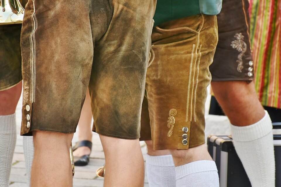 Traditionelle bayerische Trachtenhosen aus Leder, kombiniert mit weißen Socken. Die Szene zeigt mehrere Personen in festlicher Kleidung während eines Festes. | © pixabay