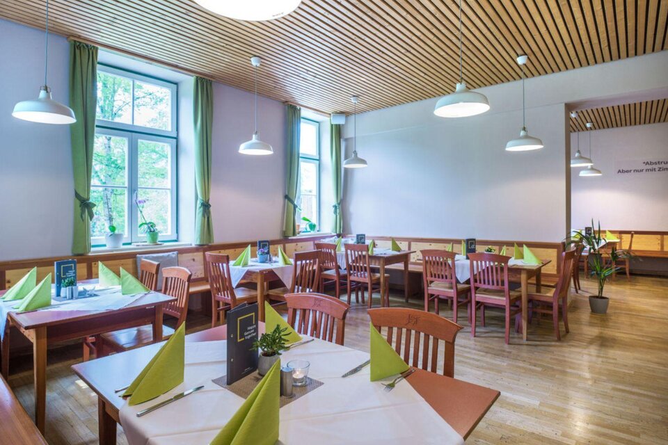 Ein helles Restaurant mit Holzmöbeln und grünen Dekorationen. Die Tische sind für Gäste vorbereitet und das Licht ist freundlich. | © JUFA Hotel Grundlsee