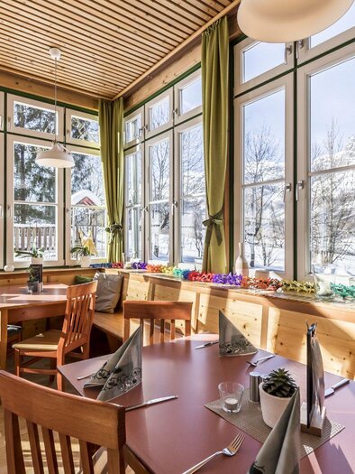 A cozy conservatory with many windows and a view of the mountains. The table is nicely set and the atmosphere is inviting. | © JUFA Grundlsee