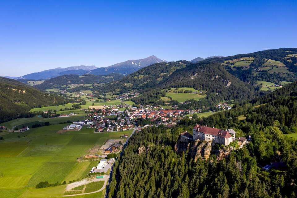 Eine malerische Landschaft mit sanften Hügeln und einem kleinen Dorf im Tal. Im Hintergrund sind die Berge und ein klarer blauer Himmel zu sehen. | © Tv Murau