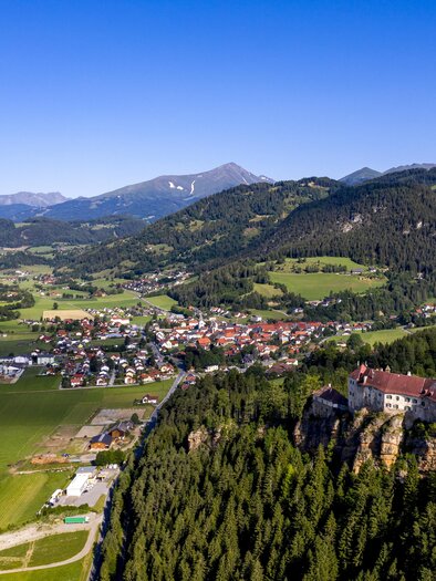 A picturesque landscape with gentle hills and a small village in the valley. In the background, the mountains and a clear blue sky can be seen. | © Tv Murau