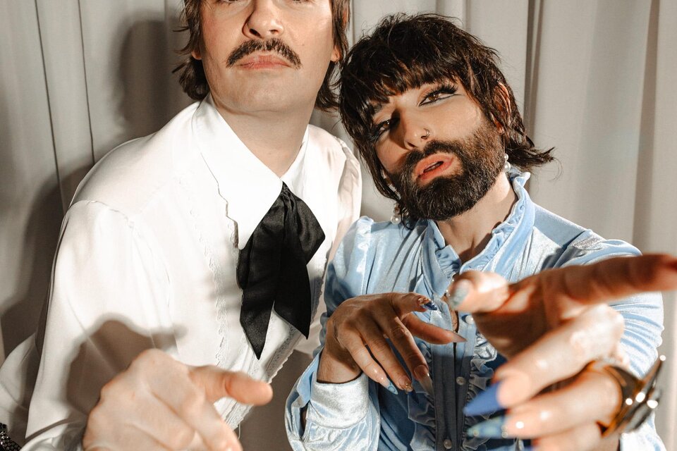 Martin Zerza als Herr Martin - in weißem Hemd, mit schwarzer Schleife und scharzer Hose - und Tom Neuwirth als Frau Martin - in hellblauem Rüschenhemd und weißer Hose, mit langen Fingernägeln, Schminke und Vollbart - präsentieren sich vor einem beigen Bühnenvorhang. | © Oststeiermark Tourismus