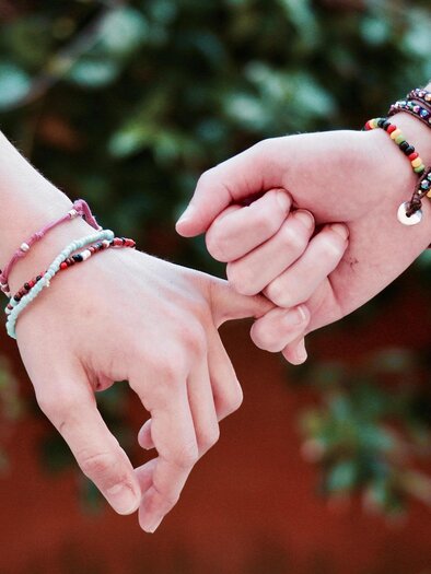 Zwei Hände halten sich gegenseitig an den Fingern. Sie sind mit bunten Armbändern geschmückt und umgeben von einer grünen Pflanzenkulisse. | © Pixabay