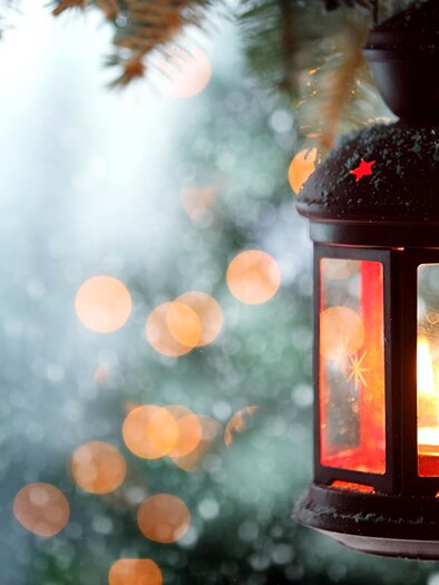 Eine rote Laterne mit einer Kerze leuchtet in der winterlichen Umgebung. Im Hintergrund sind verschwommene Lichter und Schneefall zu sehen. | © FF Graßnitz