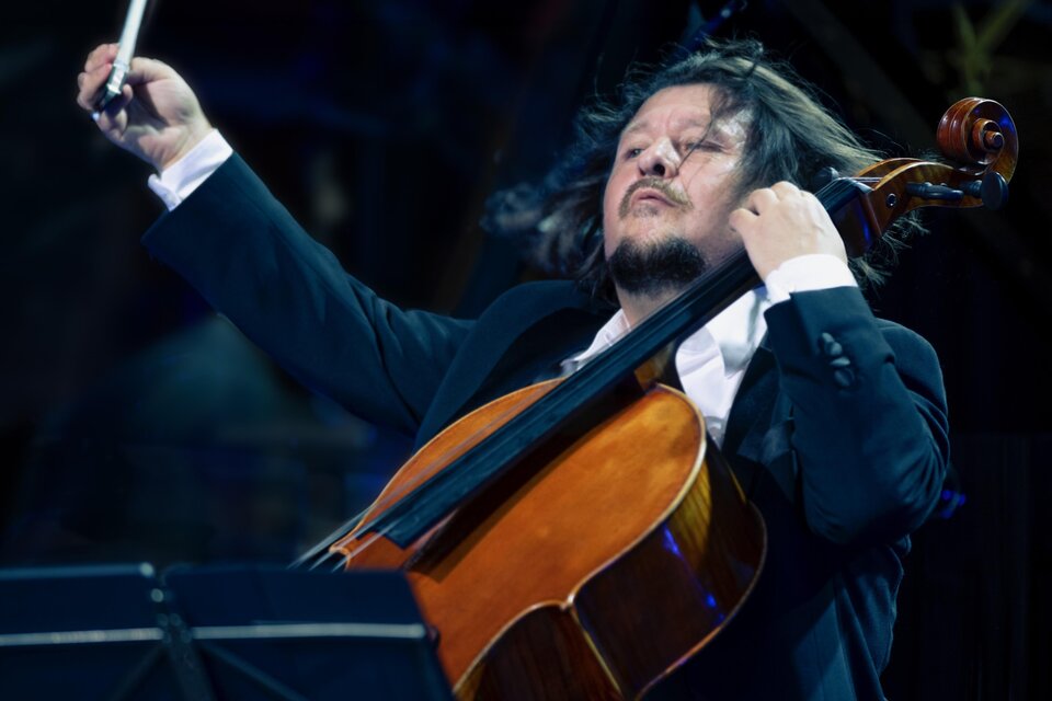Ein Musiker spielt leidenschaftlich Cello auf der Bühne. Sein Haar weht im Takt der Musik und er ist in ein elegantes schwarzes Outfit gekleidet.