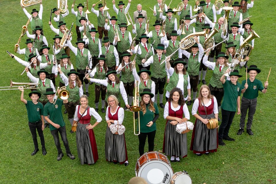 Eine große Musikgruppe in Trachten steht im Freien. Sie lächeln und posieren vor einer schönen Landschaft. | © Musikverein Stubenberg_Oststeiermark