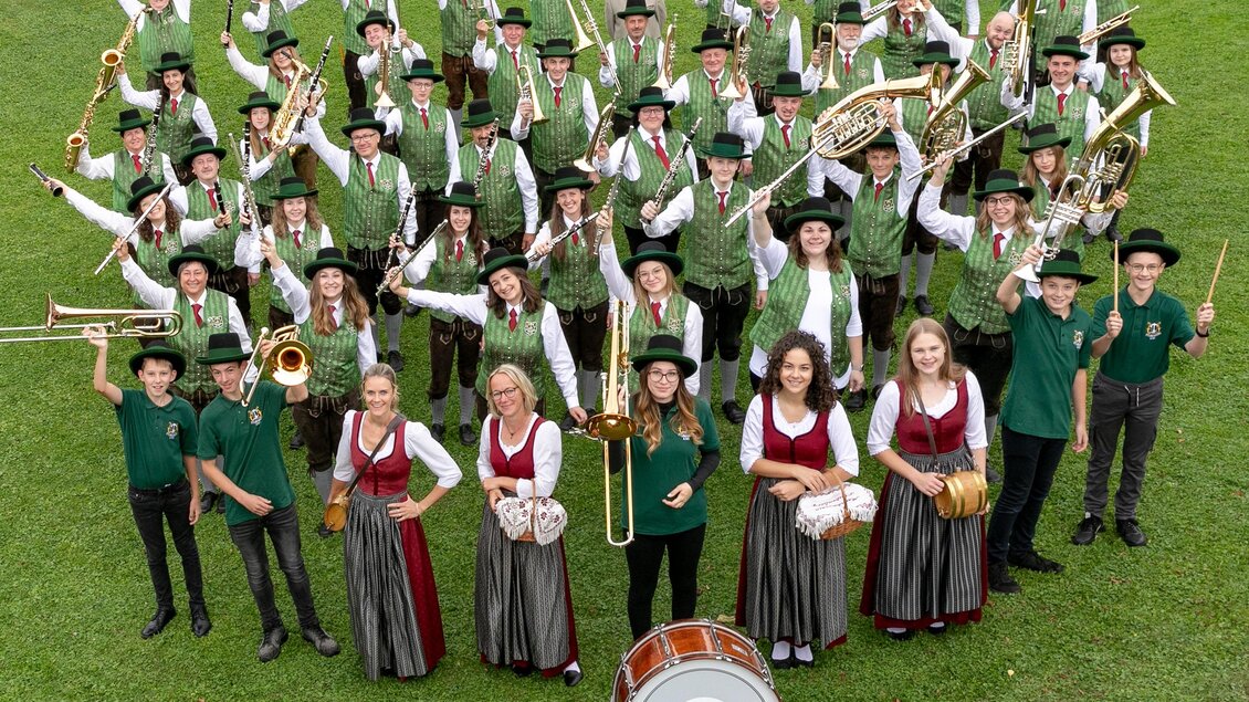 Eine große Musikgruppe in Trachten steht im Freien. Sie lächeln und posieren vor einer schönen Landschaft. | © Musikverein Stubenberg_Oststeiermark