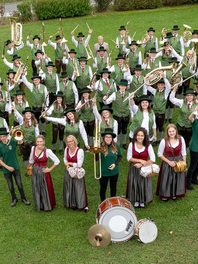 Eine große Musikgruppe in Trachten steht im Freien. Sie lächeln und posieren vor einer schönen Landschaft. | © Musikverein Stubenberg_Oststeiermark
