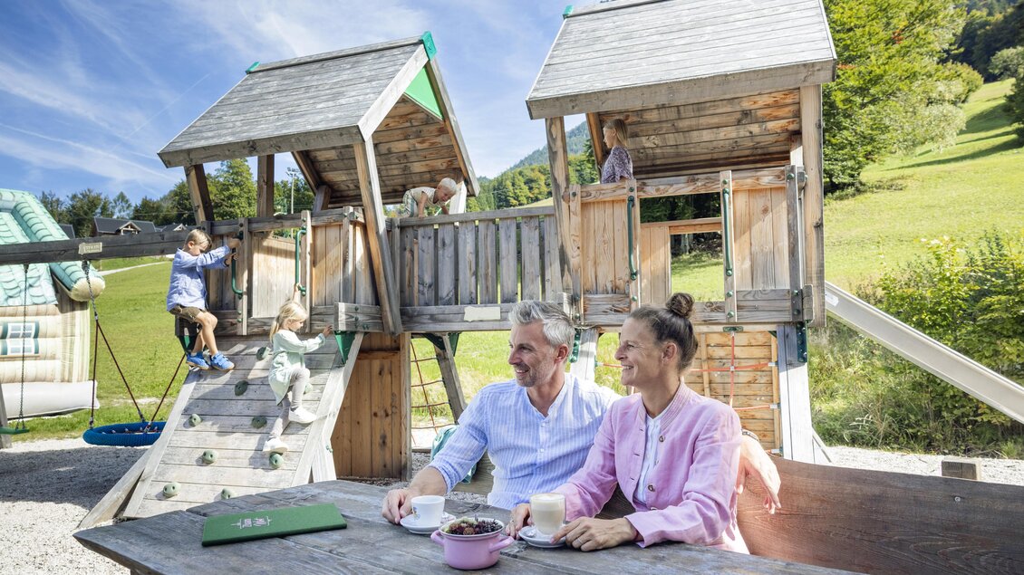 Eine Familie genießt Zeit auf einem Spielplatz mit zwei Spielhäusern. Kinder spielen begeistert und haben Spaß im Freien. | © www.zloam.at