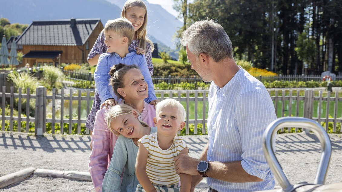 Eine Familie verbringt Zeit im Freien auf einem Spielplatz. Die Kinder lachen und spielen fröhlich mit ihrem Vater. | © www.zloam.at