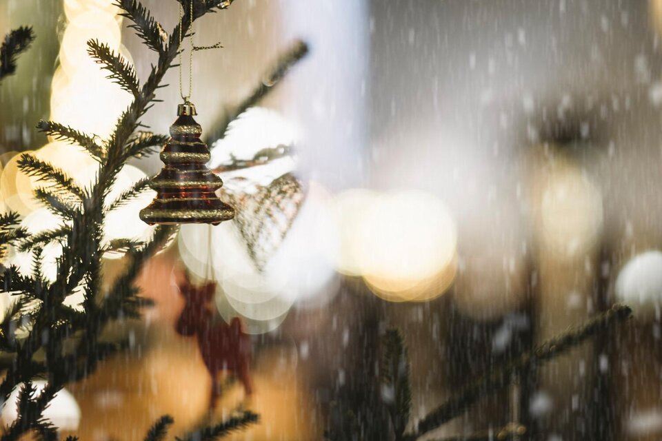 Ein schön geschmückter Weihnachtsbaum mit einer glitzernden Weihnachtskugel. Im Hintergrund fällt sanfter Schnee und die Lichter funkeln. | © Stefan Leitner