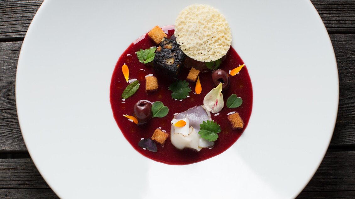 Ein kunstvoll angerichtetes Gericht auf einem weißen Teller. Es besteht aus einer roten Sauce, verschiedenen Gemüsestücken und einer knusprigen Garnitur. | © Der WILDe EDER