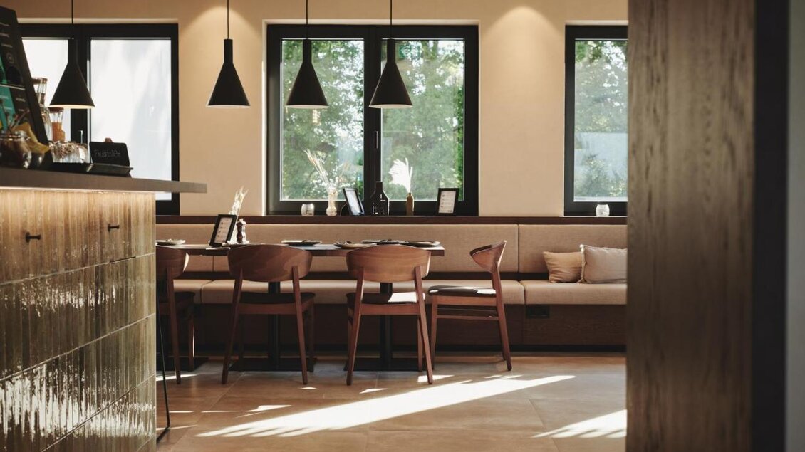 Ein modernes Café mit holzverkleideten Möbeln und großen Fenstern. Das Licht strömt sanft herein und schafft eine gemütliche Atmosphäre. | © Das Zeitwert