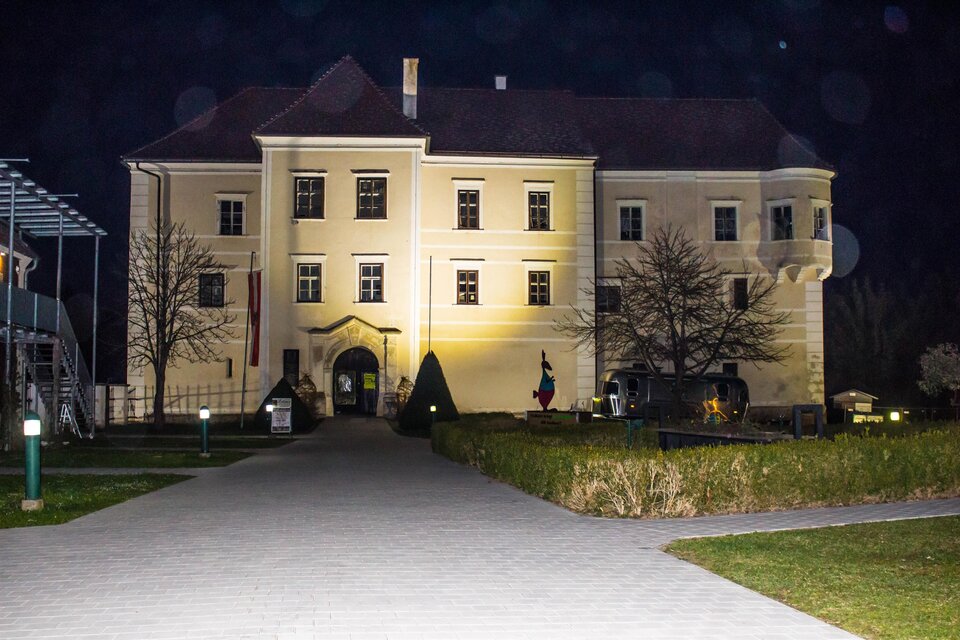 Ein historisches Gebäude bei Nacht, beleuchtet von warmem Licht. Im Vordergrund sieht man einen gepflegten Garten und Wege. | © Sandra Brünner