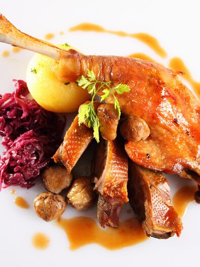Ein köstlicher Teller mit Entenkeule, serviert mit Kartoffeln, Rotkohl und einer herzhaften Soße. Das Gericht ist ansprechend dekoriert und zeigt frische Kräuter. | © AdobeStock_27014542
