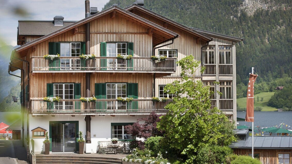 Ein charmantes Holzhaus mit mehreren Balkonen und grünen Fensterläden. Im Hintergrund sind Berge und ein See sichtbar. | © Seehotel Grundlsee