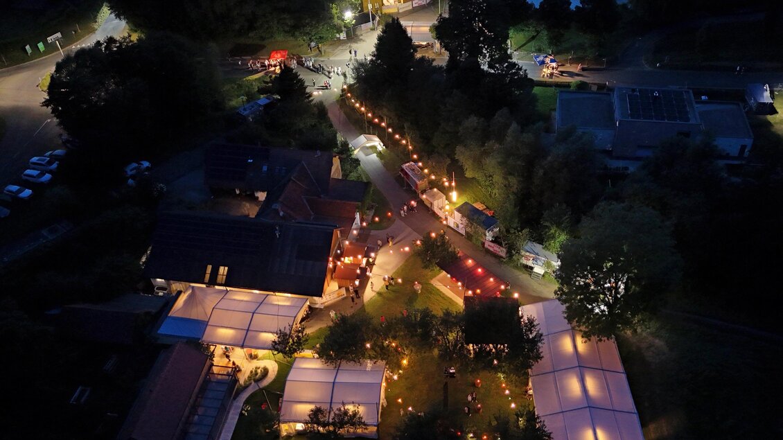Stimmungsvolle Luftaufnahme des nächtlichen Gartenfestes der Freiwilligen Feuerwehr Edersgraben bei Feldbach mit beleuchteten Zelten, Festständen und Besucherinnen und Besuchern inmitten einer idyllischen Park- und Teichlandschaft – gelebte Gemeinschaft, regionale Festkultur und besondere Sommerabende in der Erlebnisregion Thermen- & Vulkanland. | © FF Edersgraben