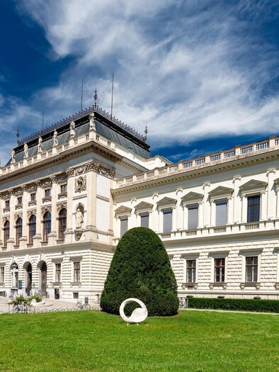 A historic building with an elegant architectural style and beautiful green gardens. The sky is blue with some clouds. | © Graz Tourismus - Harry Schiffer