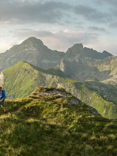 Ein atemberaubender Blick auf die Berge mit üppigem Gras im Vordergrund. Zwei Personen stehen auf einem Gipfel und genießen die Landschaft.