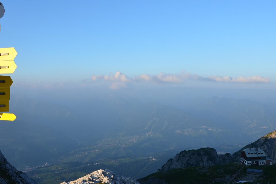 Ein atemberaubender Blick auf die Berge mit einem Wegweiser im Vordergrund. Der Himmel ist klar und die Landschaft erstreckt sich bis zum Horizont. | © Tourismusverband Schladming-Dachstein/Erlebnisregion Schladming-Dachstein