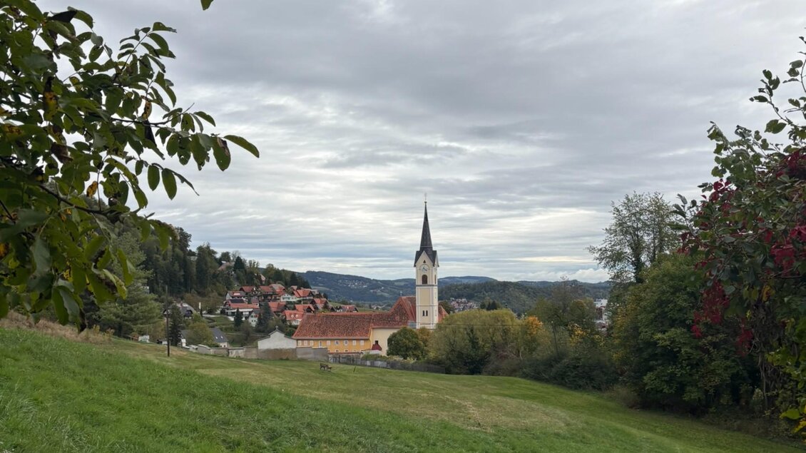 Blick über eine grüne Wiese auf die Wallfahrtskirche Maria Lankowitz mit ihrem Kirchturm, umgeben von Häusern und Hügeln. | © Kohlbacher