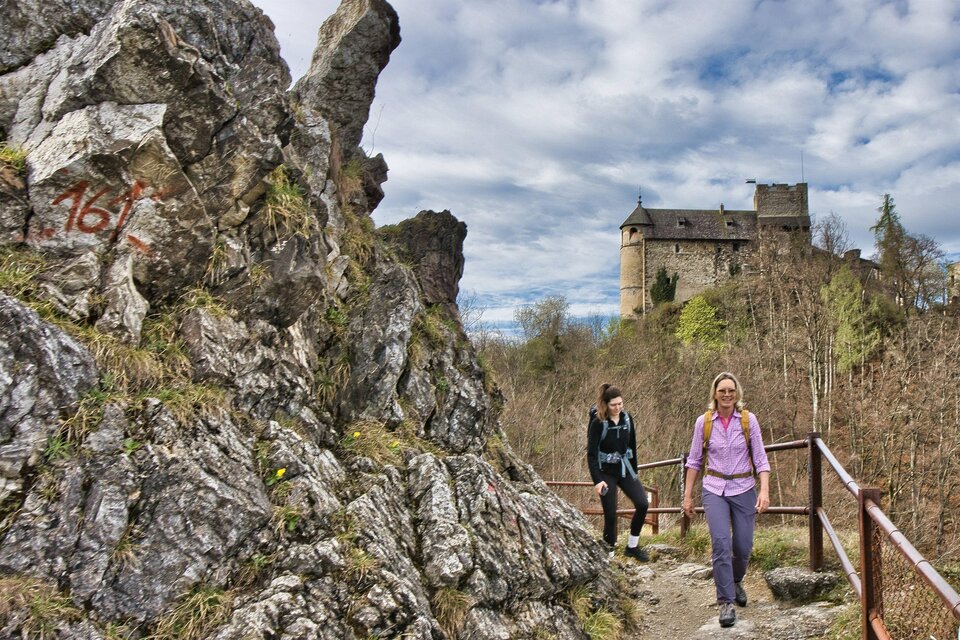 Zwei Wanderinnen auf einem felsigen Weg mit Geländer, im Hintergrund die mittelalterliche Burgruine Gösting. | © Weges