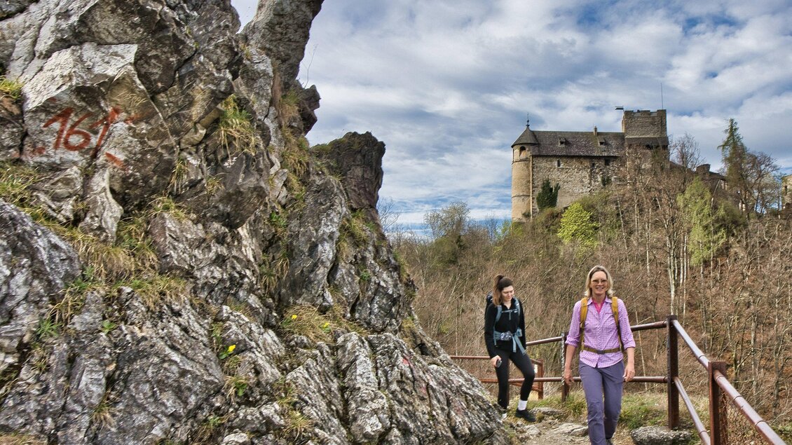 Zwei Wanderinnen auf einem felsigen Weg mit Geländer, im Hintergrund die mittelalterliche Burgruine Gösting. | © Weges