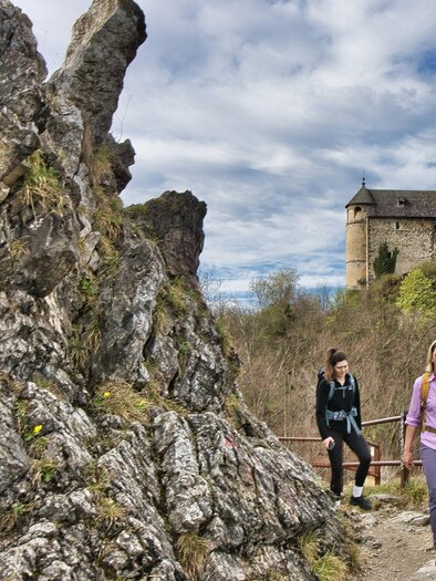 Two female hikers on a rocky path with railing, in the background the medieval castle ruins of Goesting. | © Weges