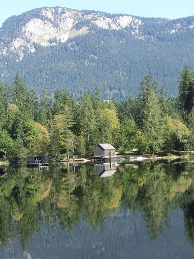 A lake is located in the middle of the forest, and along the shore there are isolated small boathouses, and a bathing jetty leads into the water. | © Daniela Casari
