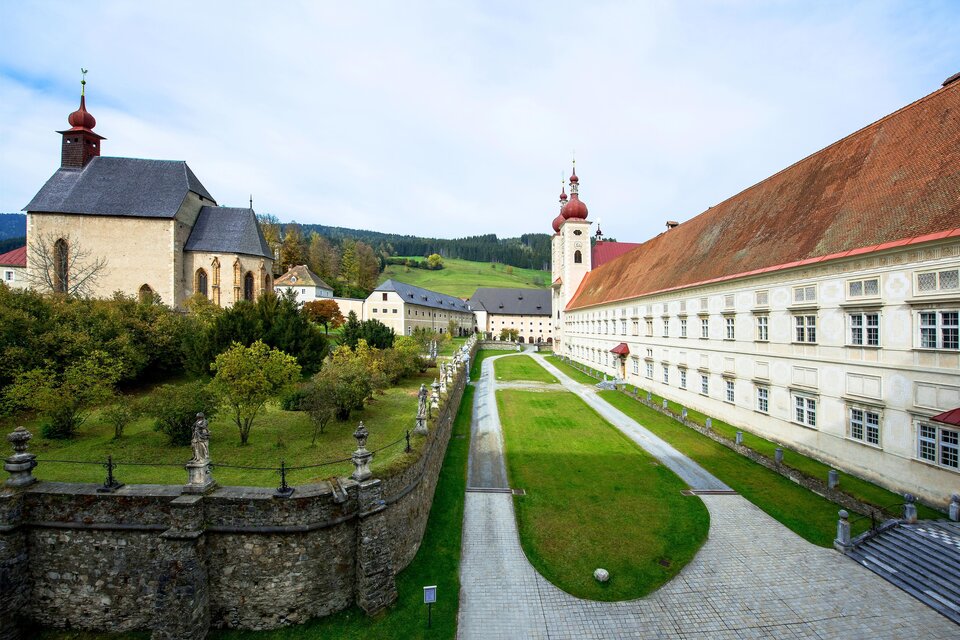 Eine historische Klosteranlage mit beeindruckenden Gebäuden und einem gepflegten Garten. Sanfte Hügel im Hintergrund vervollständigen die malerische Szenerie. | © Tv Murau