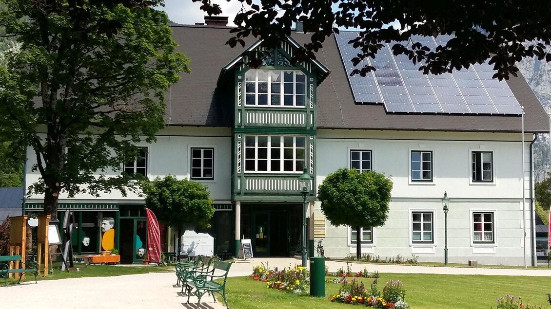 Ein hübsches Gebäude mit grünen Akzenten und Solarpanels auf dem Dach. Der Garten ist gepflegt und einladend mit bunten Blumen und Sitzbänken. | © Petra Kirchschlager