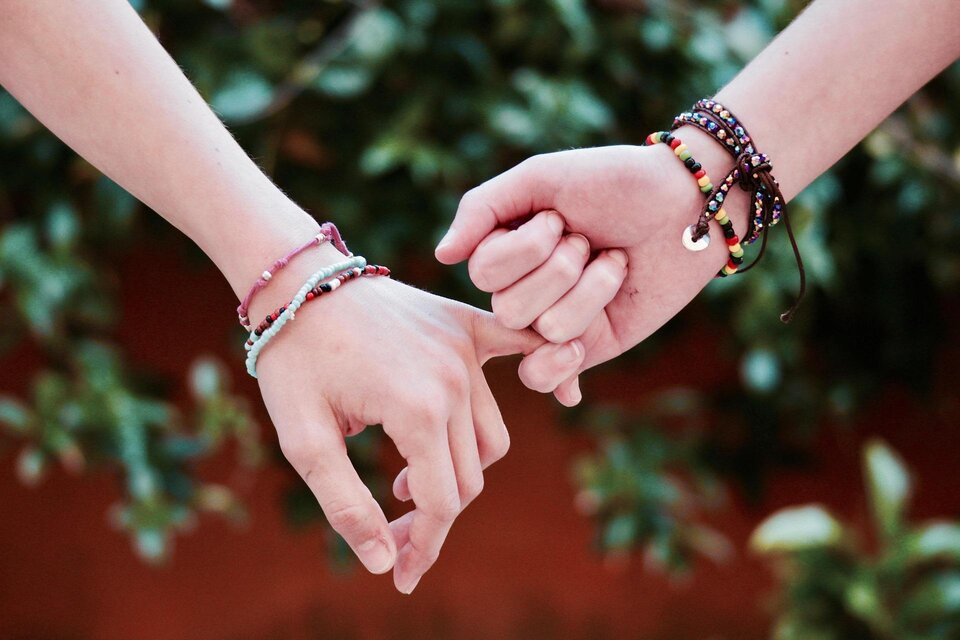 Zwei Hände halten sich fest, geschmückt mit bunten Armbändern. Der Hintergrund zeigt grüne Blätter, die eine freundliche Atmosphäre schaffen. | © pixabay