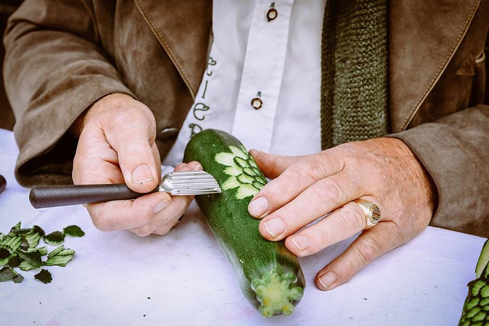 Eine Person schnitzt mit einem speziellen Werkzeug ein Muster in eine Zucchini. Grünes Gemüse wird kreativ bearbeitet. | © Foto Freisinger